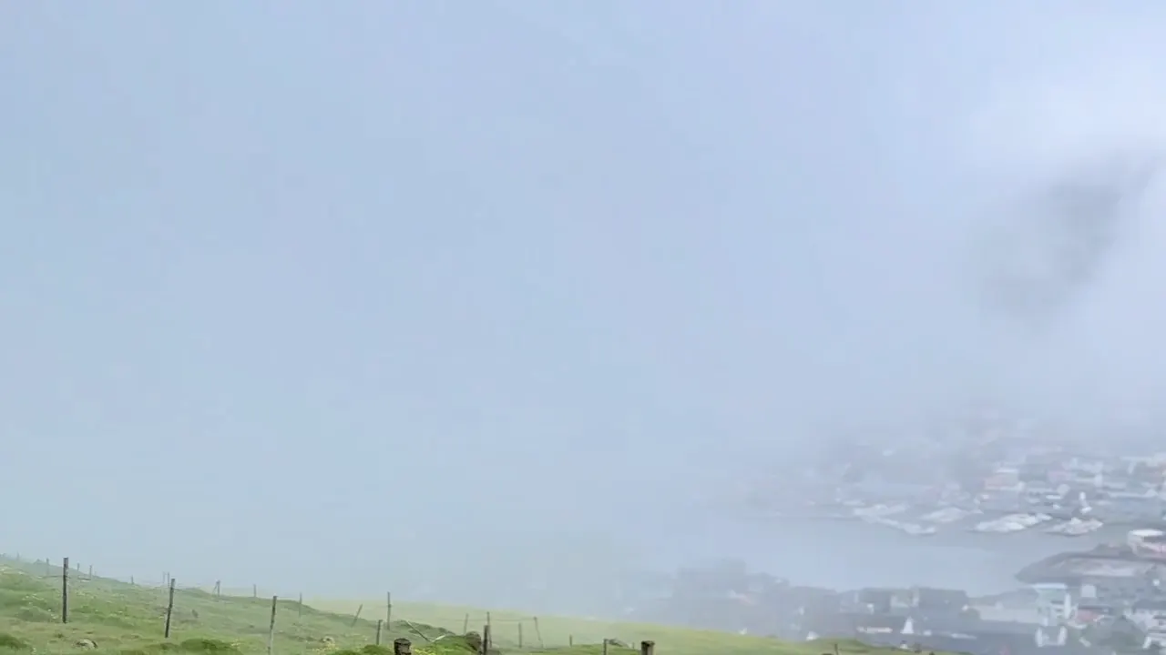 Fog over a Faroe Islands coastal village, seen from a grassy hillside